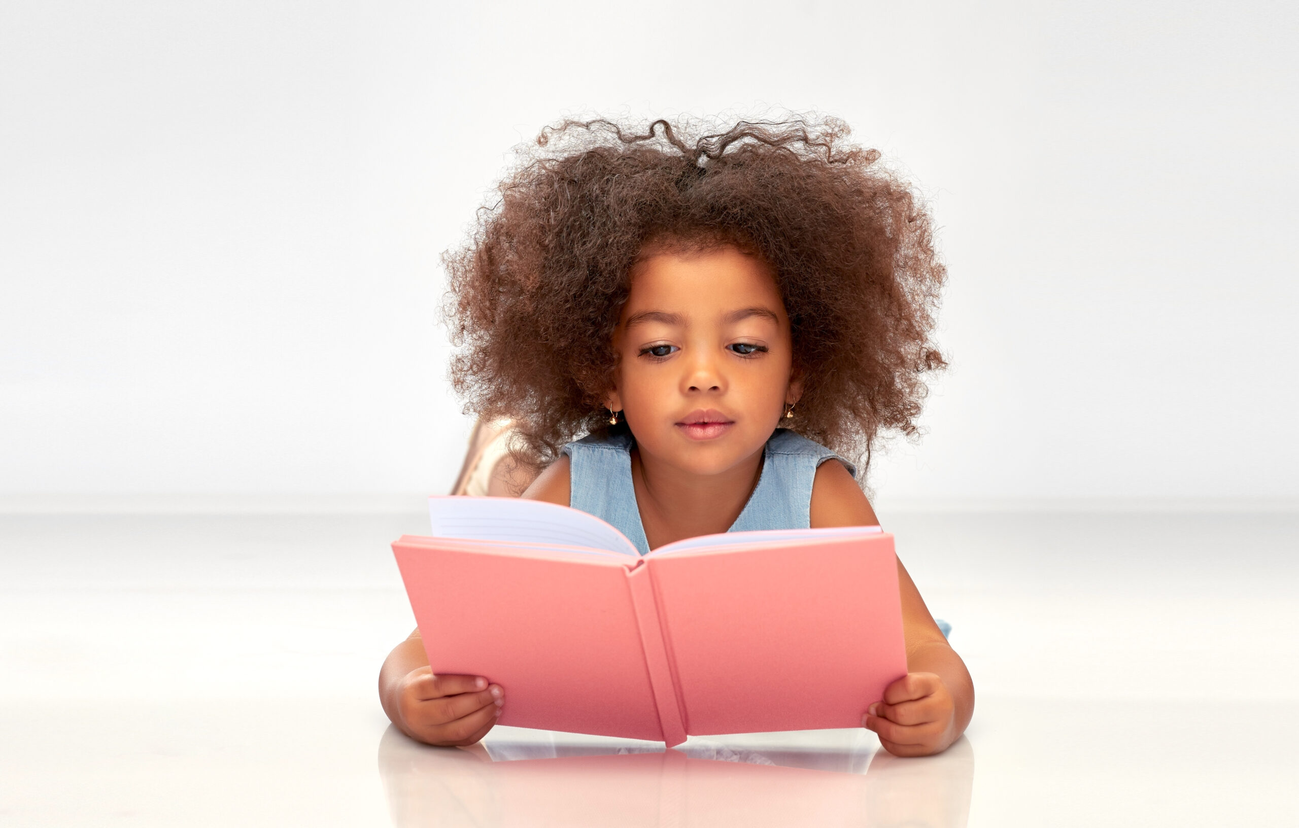 childhood, school and education concept - little african american girl reading book over grey background